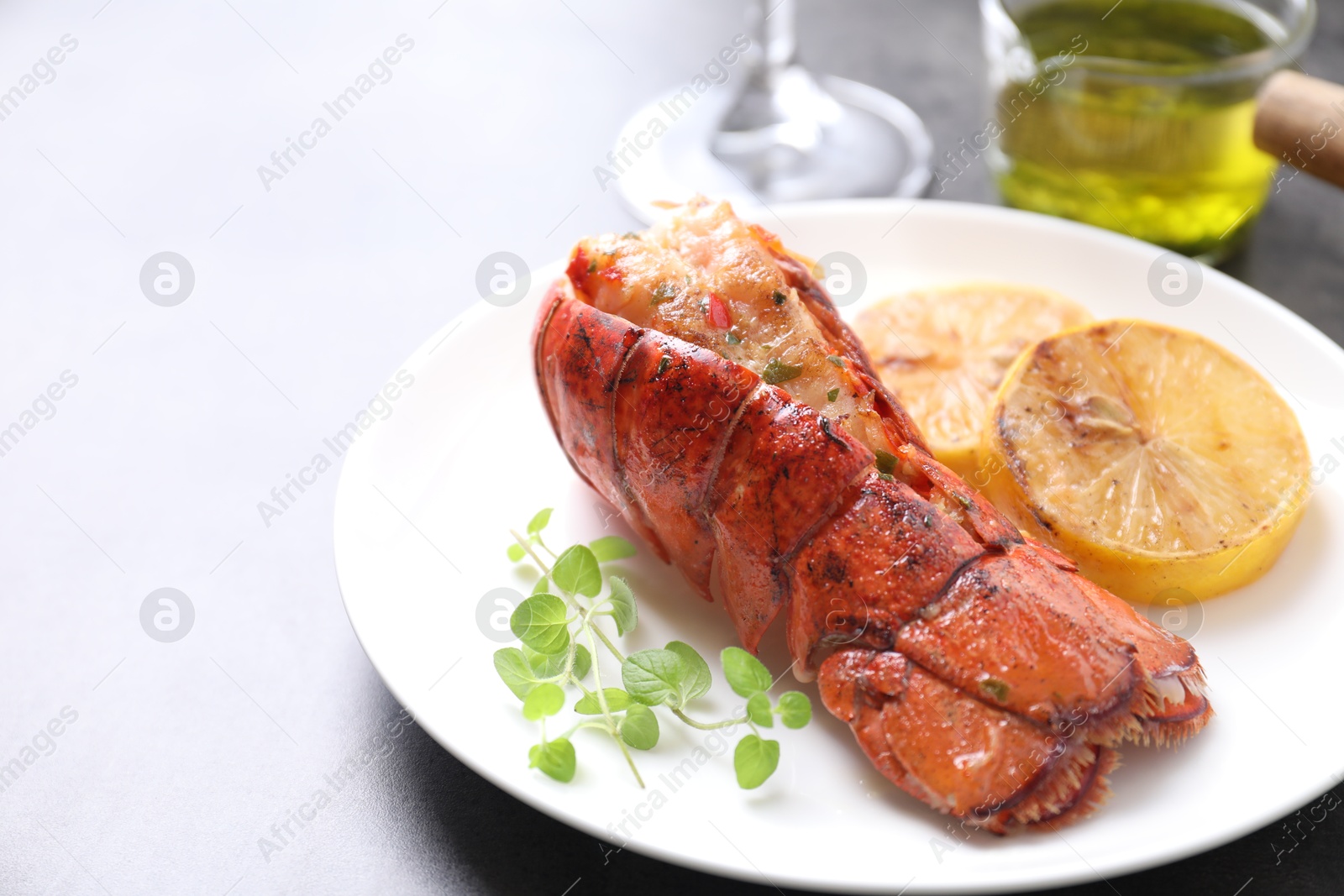 Photo of Delicious lobster tail with microgreens and slices of lemon on grey table, closeup. Space for text