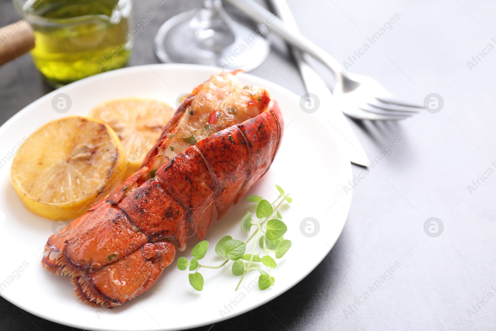 Photo of Delicious lobster tail with microgreens and slices of lemon on grey table, closeup. Space for text