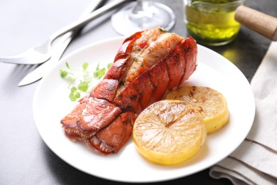 Photo of Delicious lobster tail with microgreens and slices of lemon on grey table, closeup