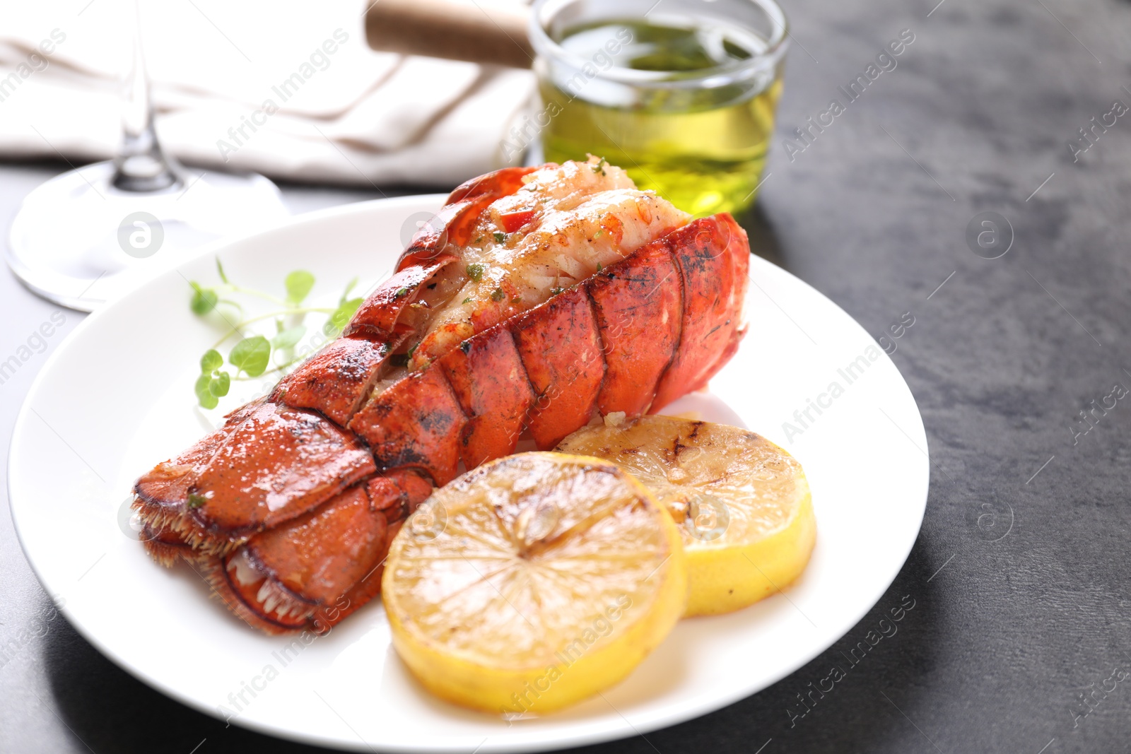 Photo of Delicious lobster tail with microgreens and slices of lemon on grey textured table, closeup