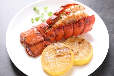 Photo of Delicious lobster tail with microgreens and slices of lemon on grey textured table, closeup