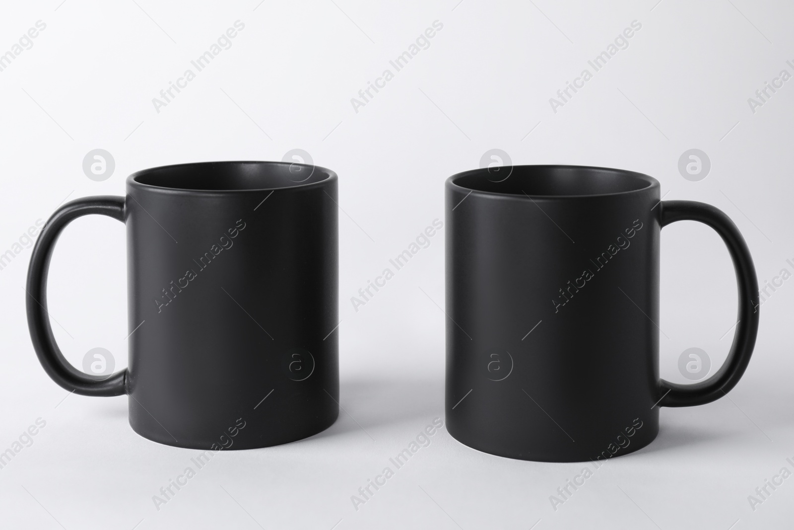 Photo of Two blank black mugs on white background. Mockup for design