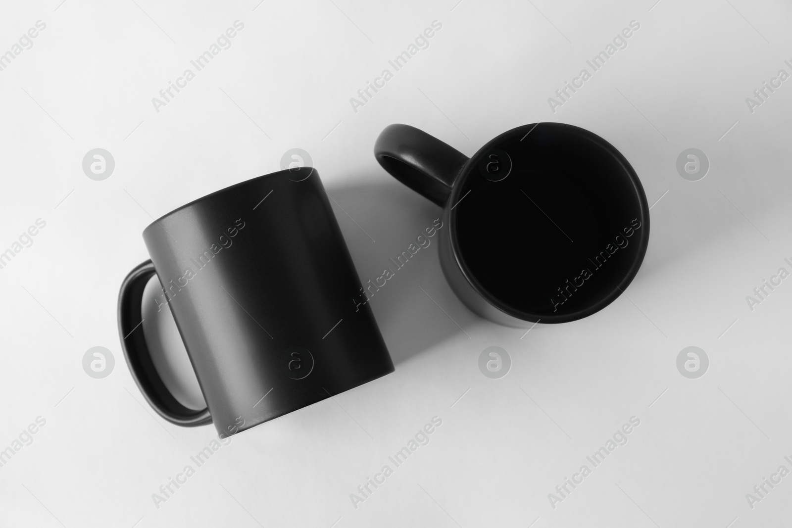 Photo of Two blank black mugs on white background, top view. Mockup for design