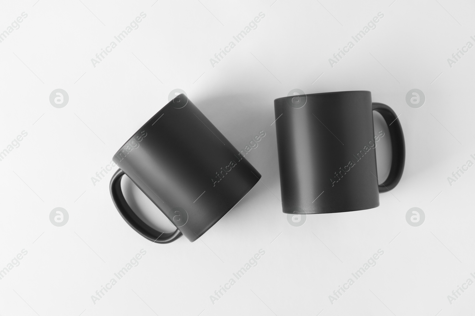 Photo of Two blank black mugs on white background, top view. Mockup for design