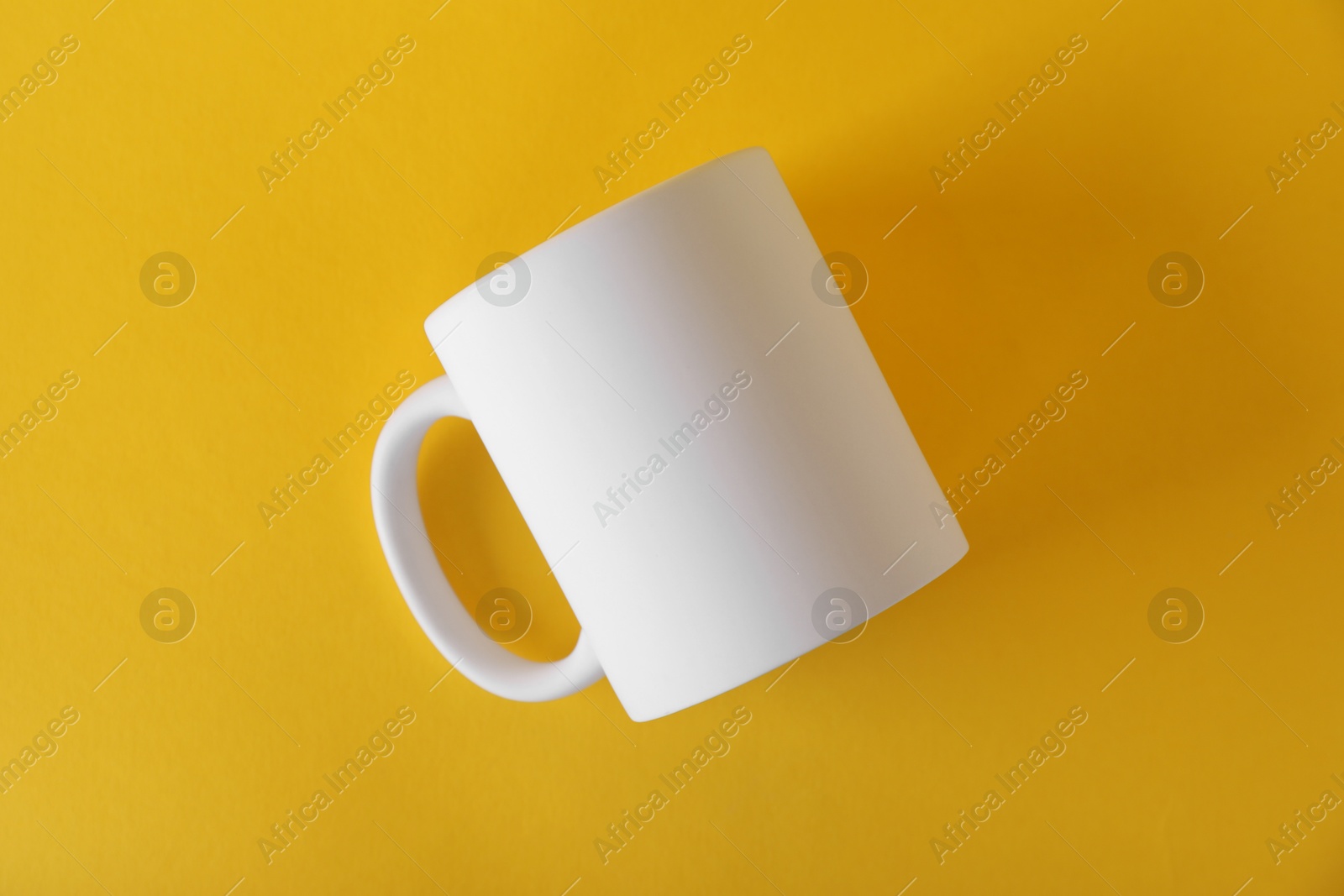 Photo of One blank white mug on yellow background, top view. Mockup for design