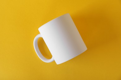 Photo of One blank white mug on yellow background, top view. Mockup for design