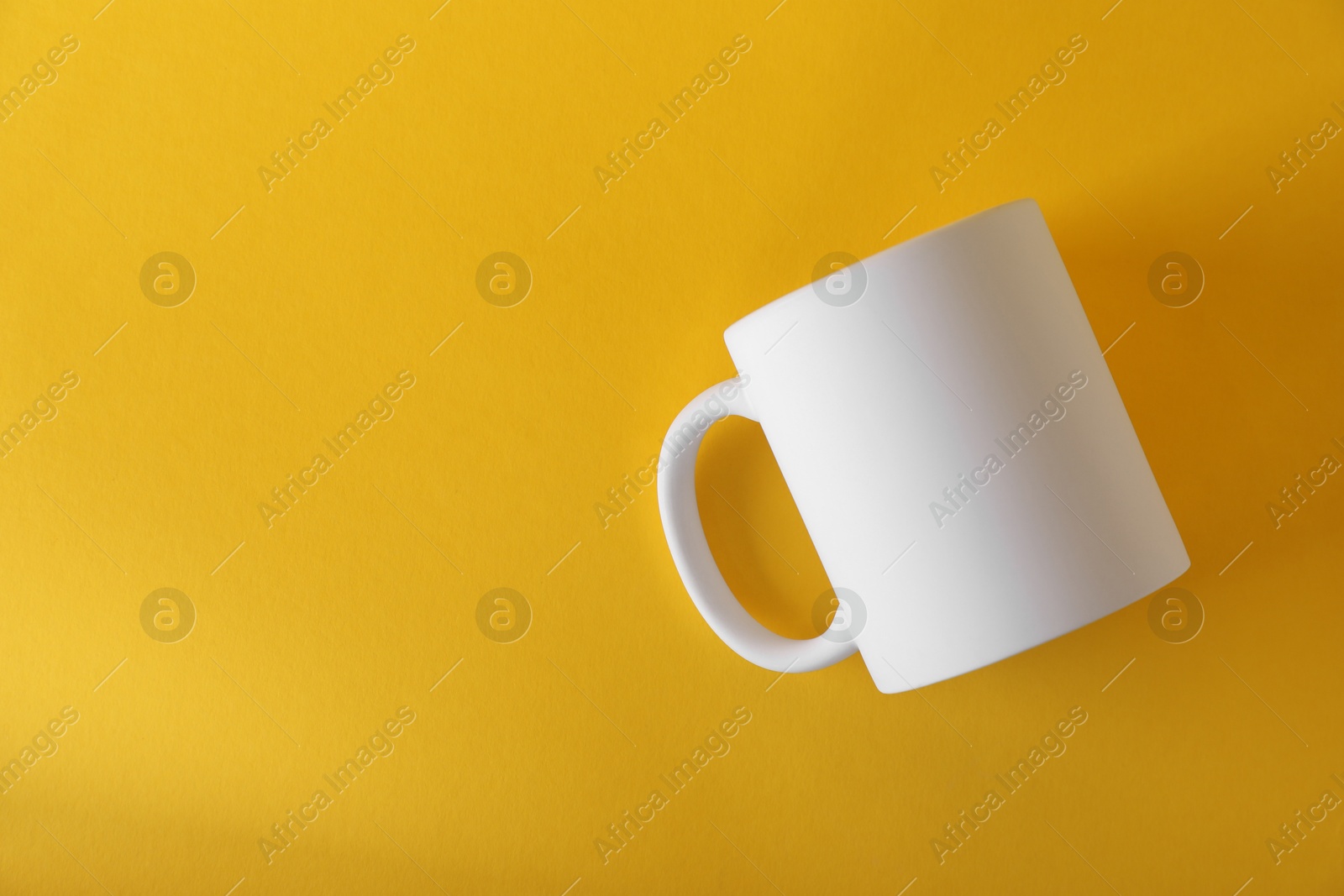 Photo of One blank white mug on yellow background, top view. Mockup for design