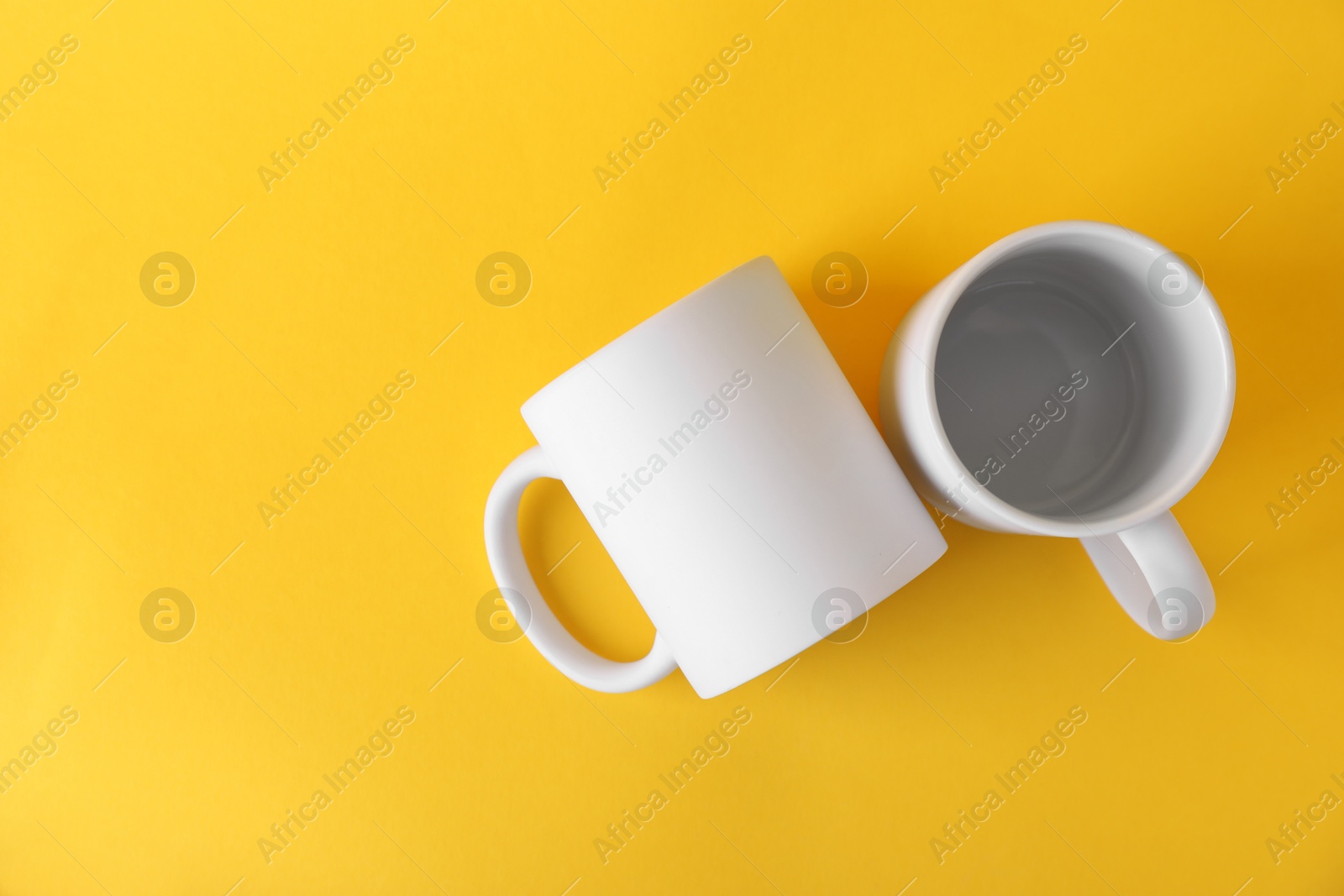 Photo of Two blank white mugs on yellow background, top view. Mockup for design