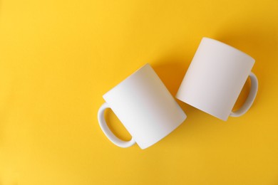 Photo of Two blank white mugs on yellow background, top view. Mockup for design