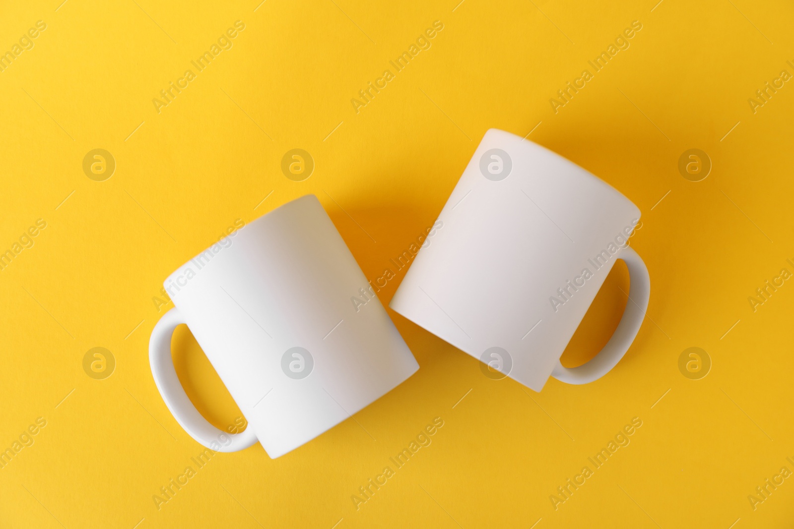 Photo of Two blank white mugs on yellow background, top view. Mockup for design