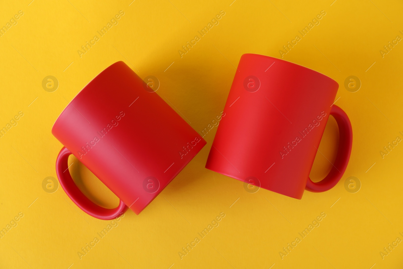 Photo of Two blank red mugs on yellow background, top view. Mockup for design