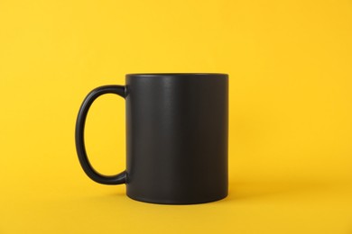 Photo of One blank black mug on yellow background. Mockup for design