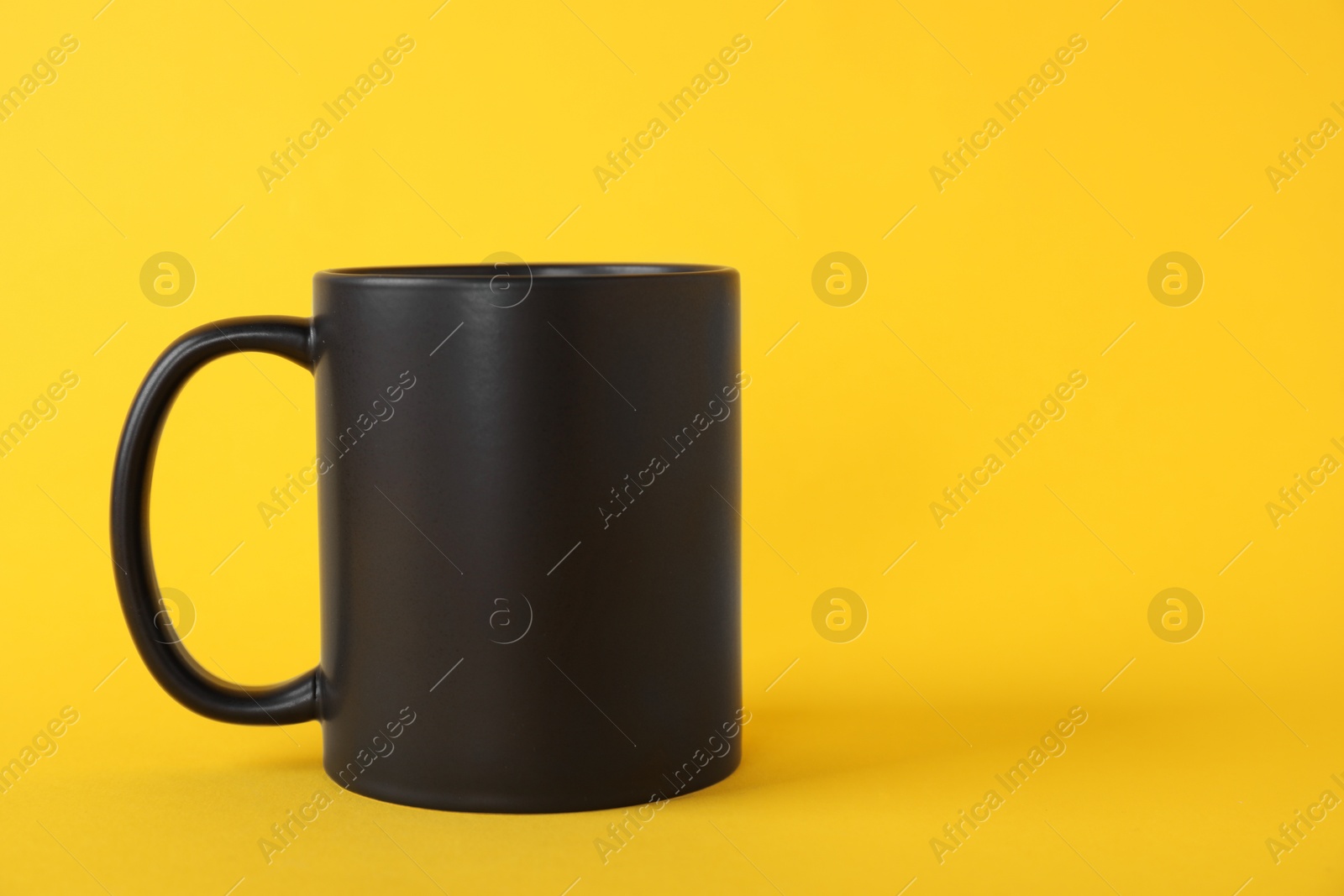 Photo of One blank black mug on yellow background. Mockup for design