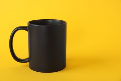 Photo of One blank black mug on yellow background. Mockup for design