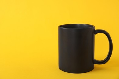 Photo of One blank black mug on yellow background. Mockup for design