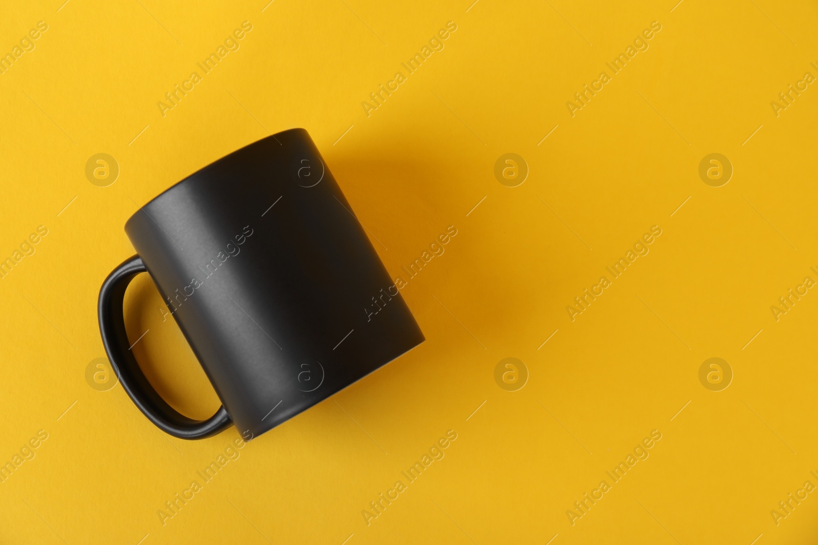 Photo of One blank black mug on yellow background, top view. Mockup for design