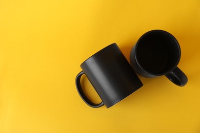 Photo of Two blank black mugs on yellow background, top view. Mockup for design