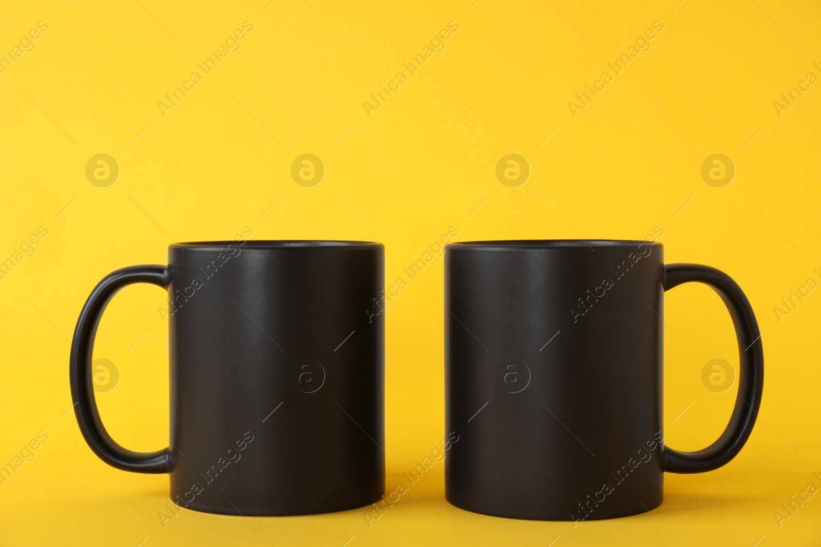 Photo of Two blank black mugs on yellow background. Mockup for design