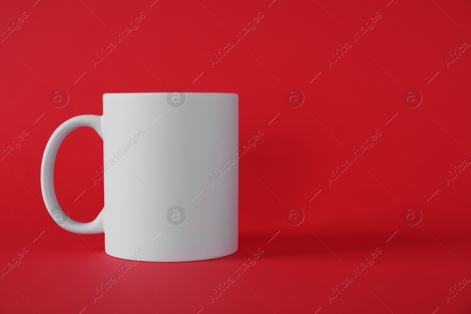 Photo of One blank white mug on red background. Mockup for design