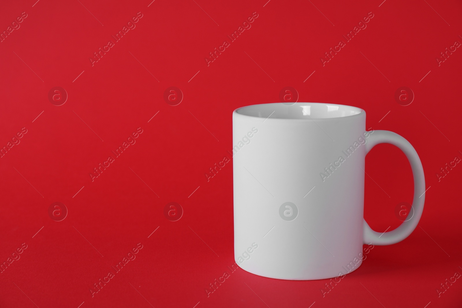 Photo of One blank white mug on red background. Mockup for design