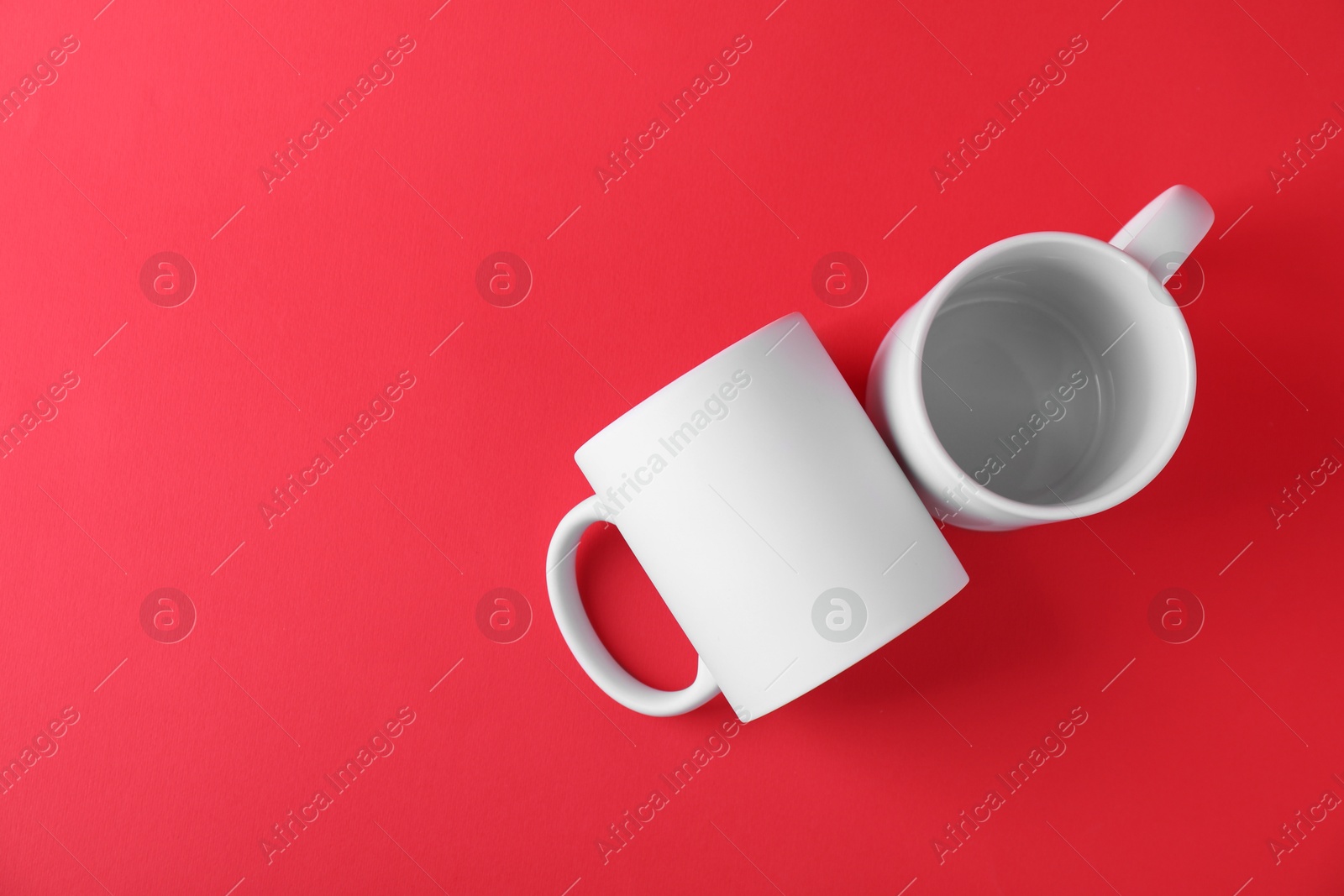 Photo of Two blank white mugs on red background, top view. Mockup for design