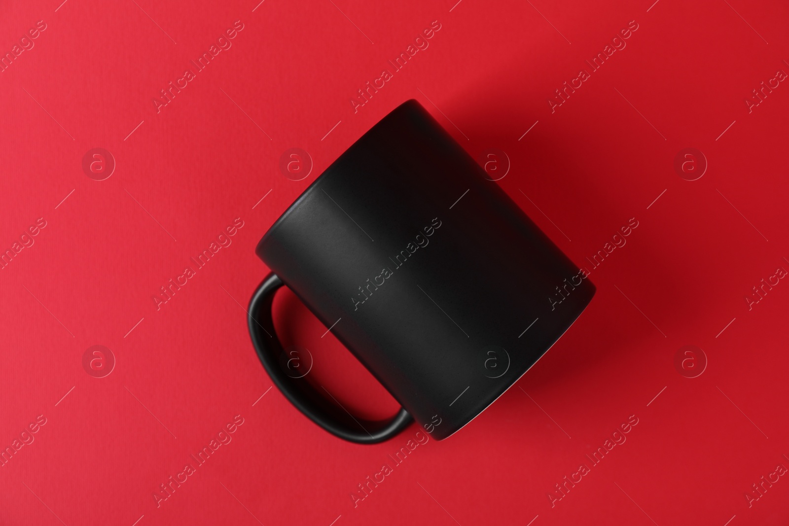 Photo of One blank black mug on red background. Mockup for design