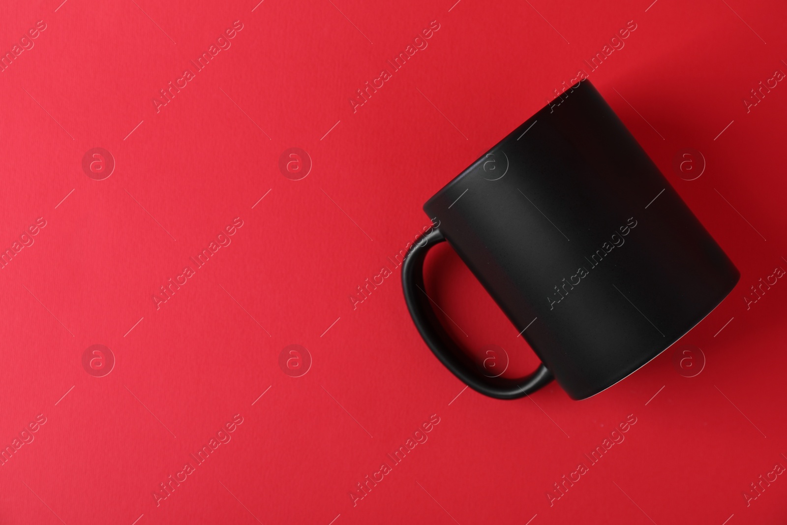 Photo of One blank black mug on red background. Mockup for design