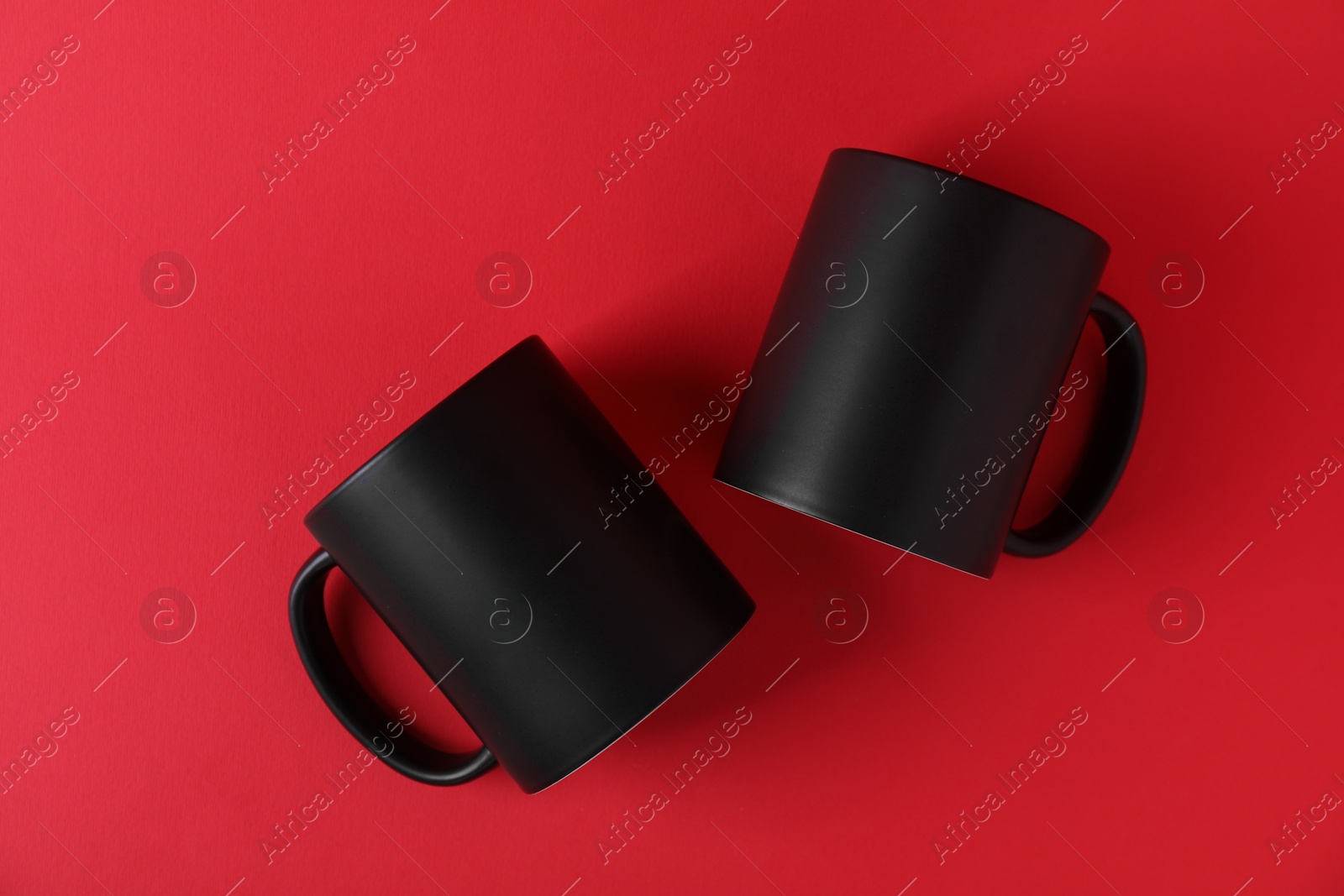 Photo of Two blank black mugs on red background, top view. Mockup for design