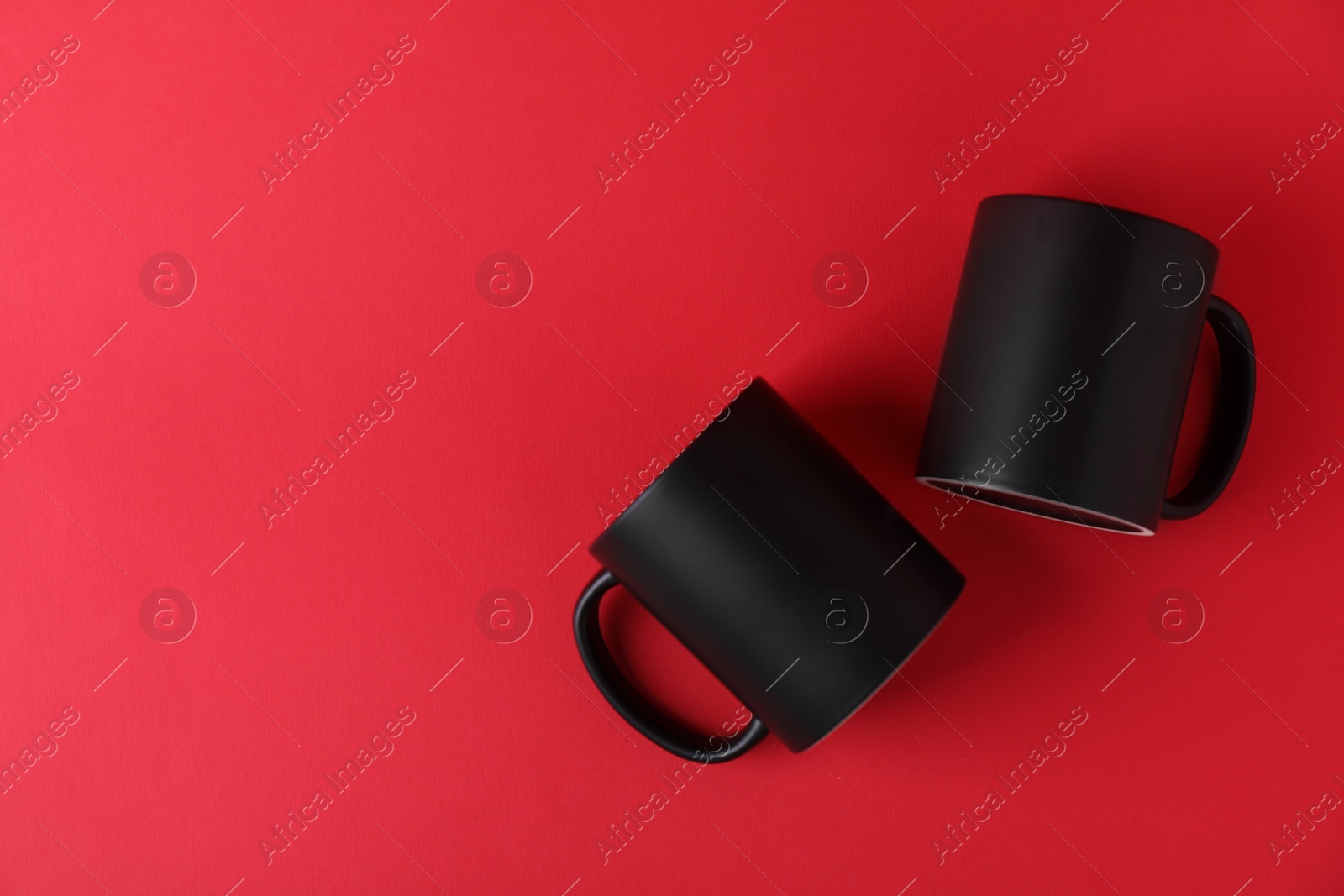 Photo of Two blank black mugs on red background, top view. Mockup for design