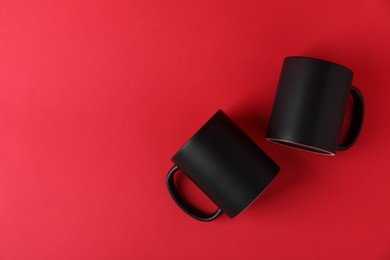 Photo of Two blank black mugs on red background, top view. Mockup for design