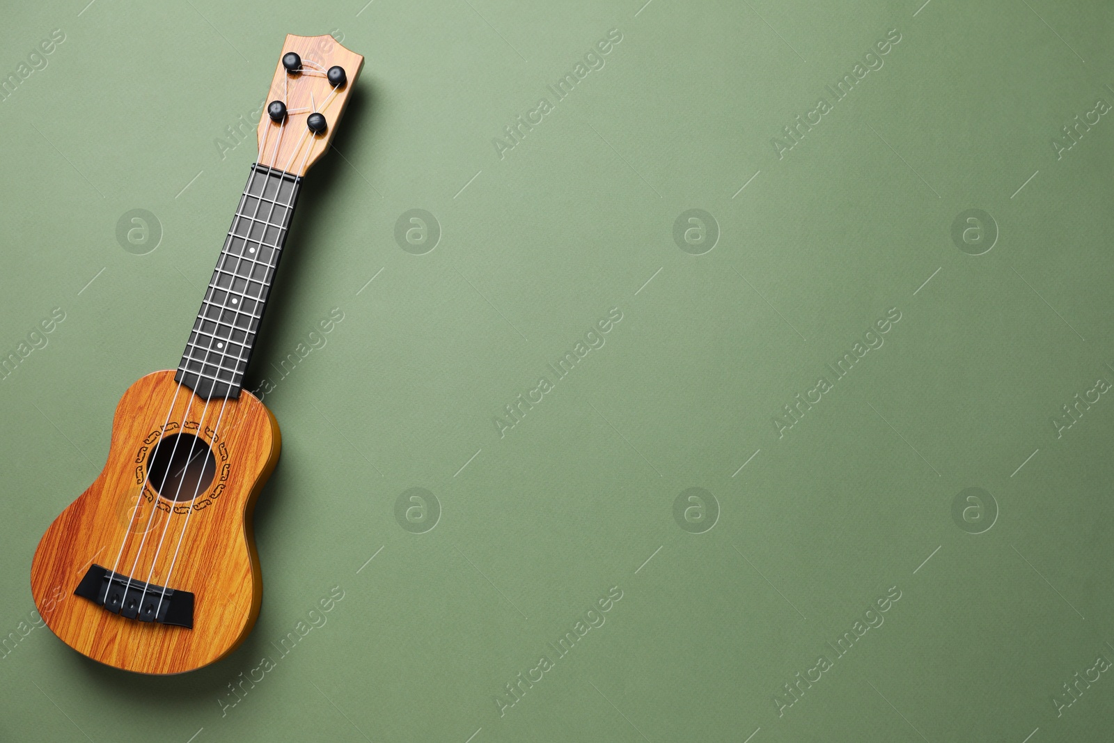 Photo of One ukulele on green background, top view. Space for text