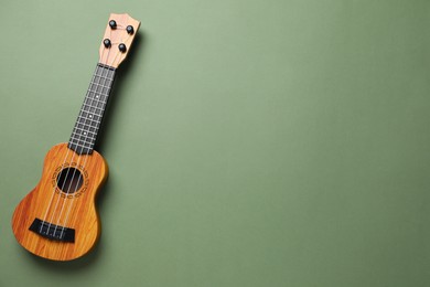 Photo of One ukulele on green background, top view. Space for text