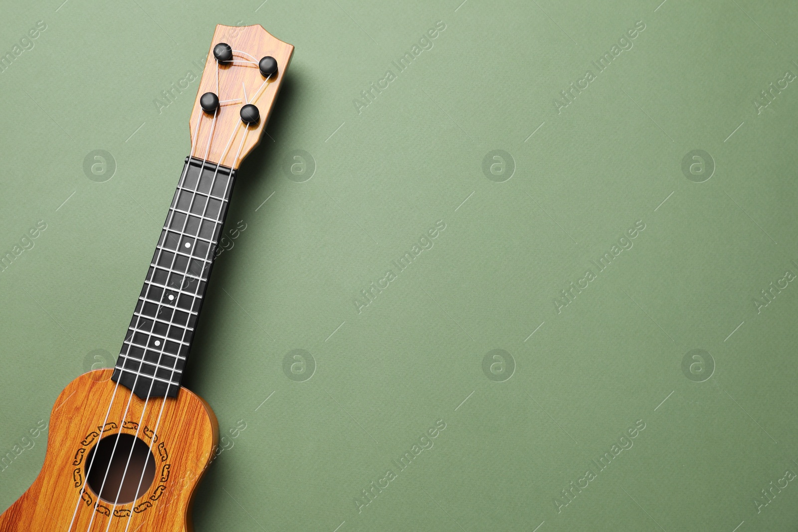 Photo of One ukulele on green background, top view. Space for text