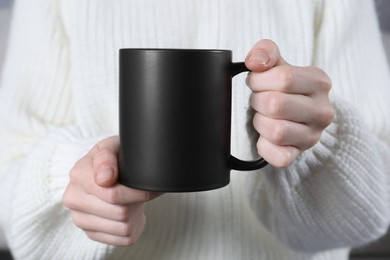 Photo of Woman holding blank black ceramic mug, closeup. Mockup for design