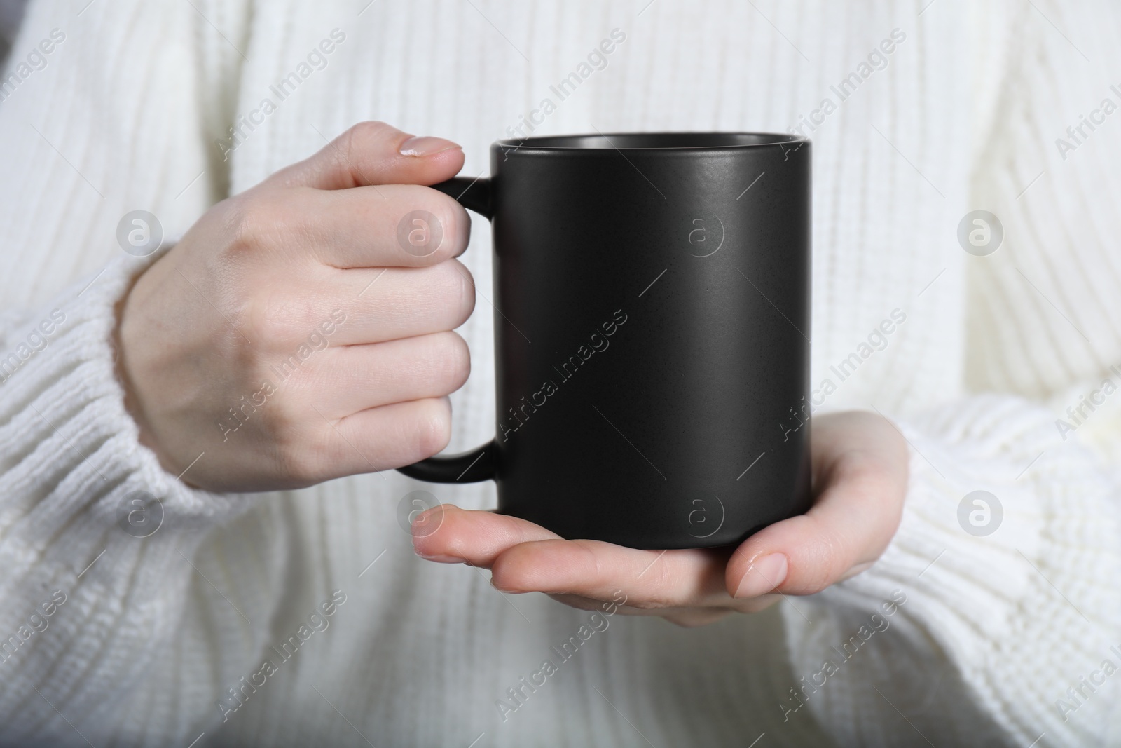 Photo of Woman holding blank black ceramic mug, closeup. Mockup for design