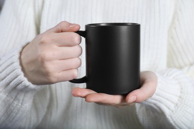 Photo of Woman holding blank black ceramic mug, closeup. Mockup for design