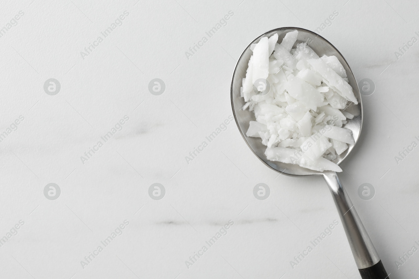 Photo of Soy wax in spoon on white marble table, top view. Space for text