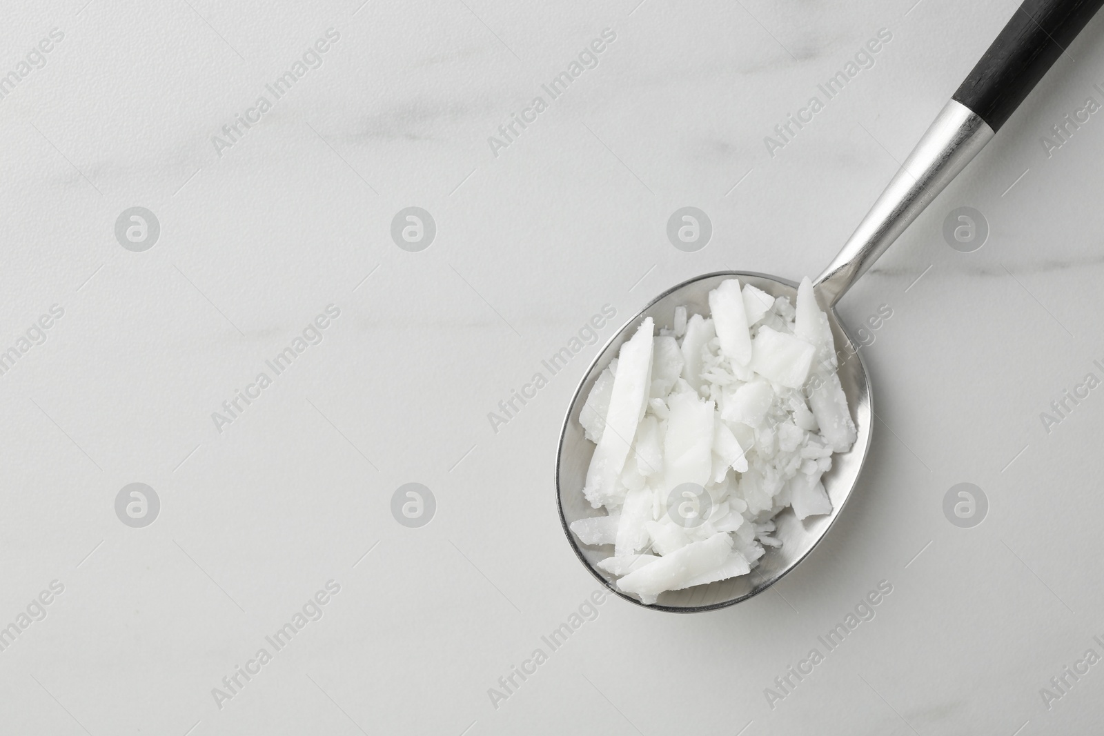 Photo of Soy wax in spoon on white marble table, top view. Space for text