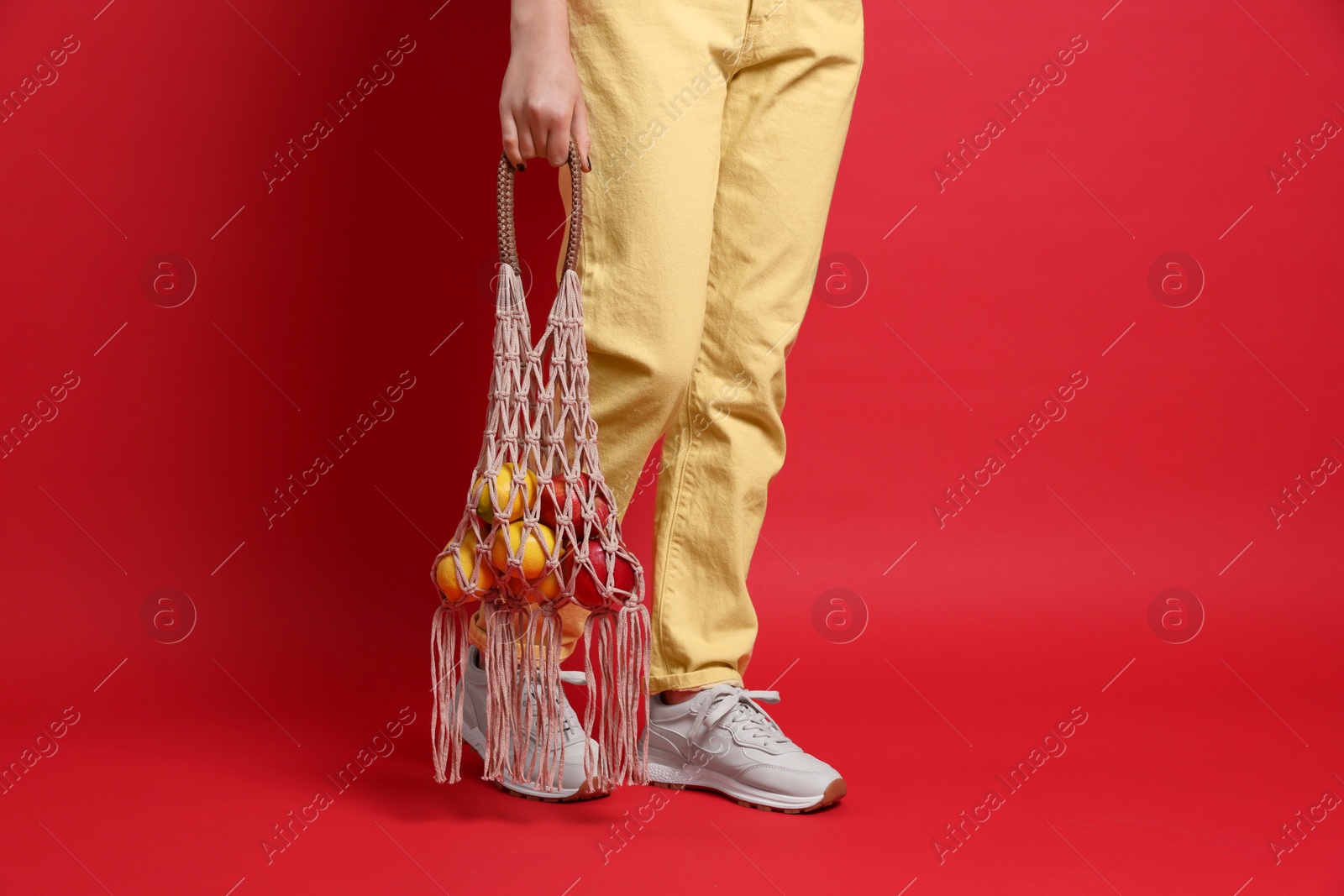 Photo of Teenage girl with handmade macrame bag on red background, closeup