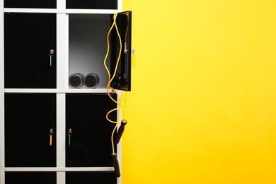 Photo of Open locker with dumbbells and skipping rope on orange background, space for text