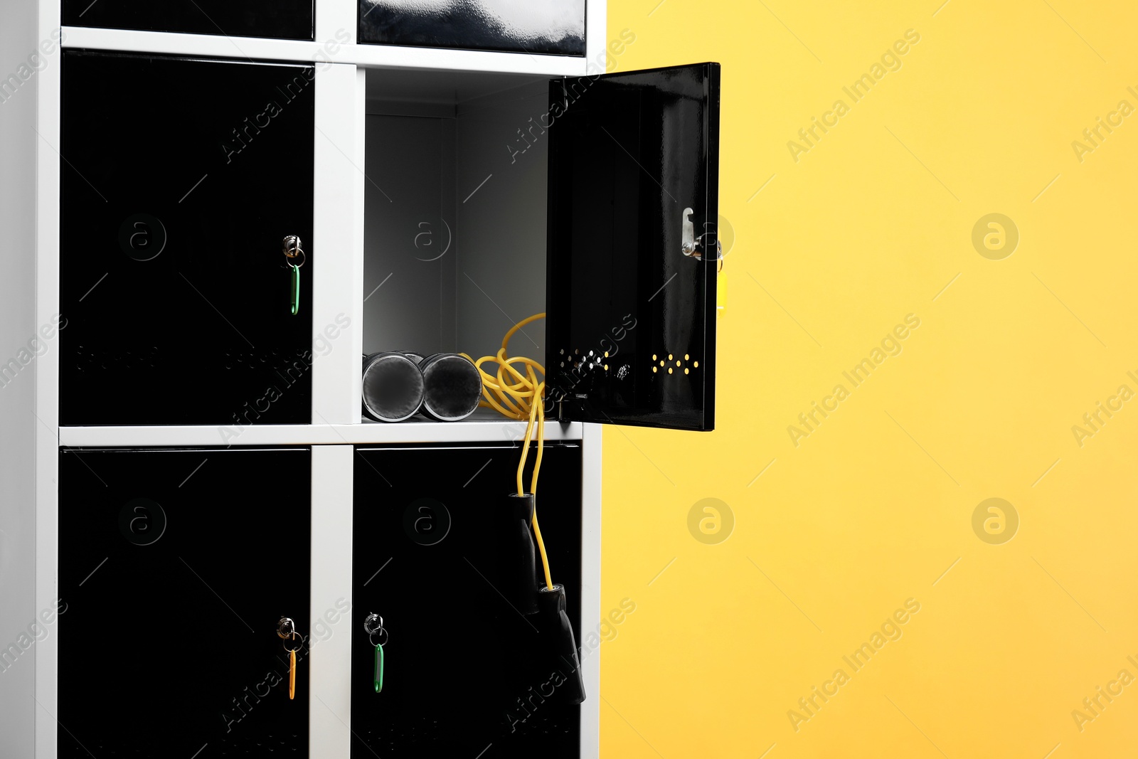 Photo of Open locker with dumbbells and skipping rope on orange background, space for text