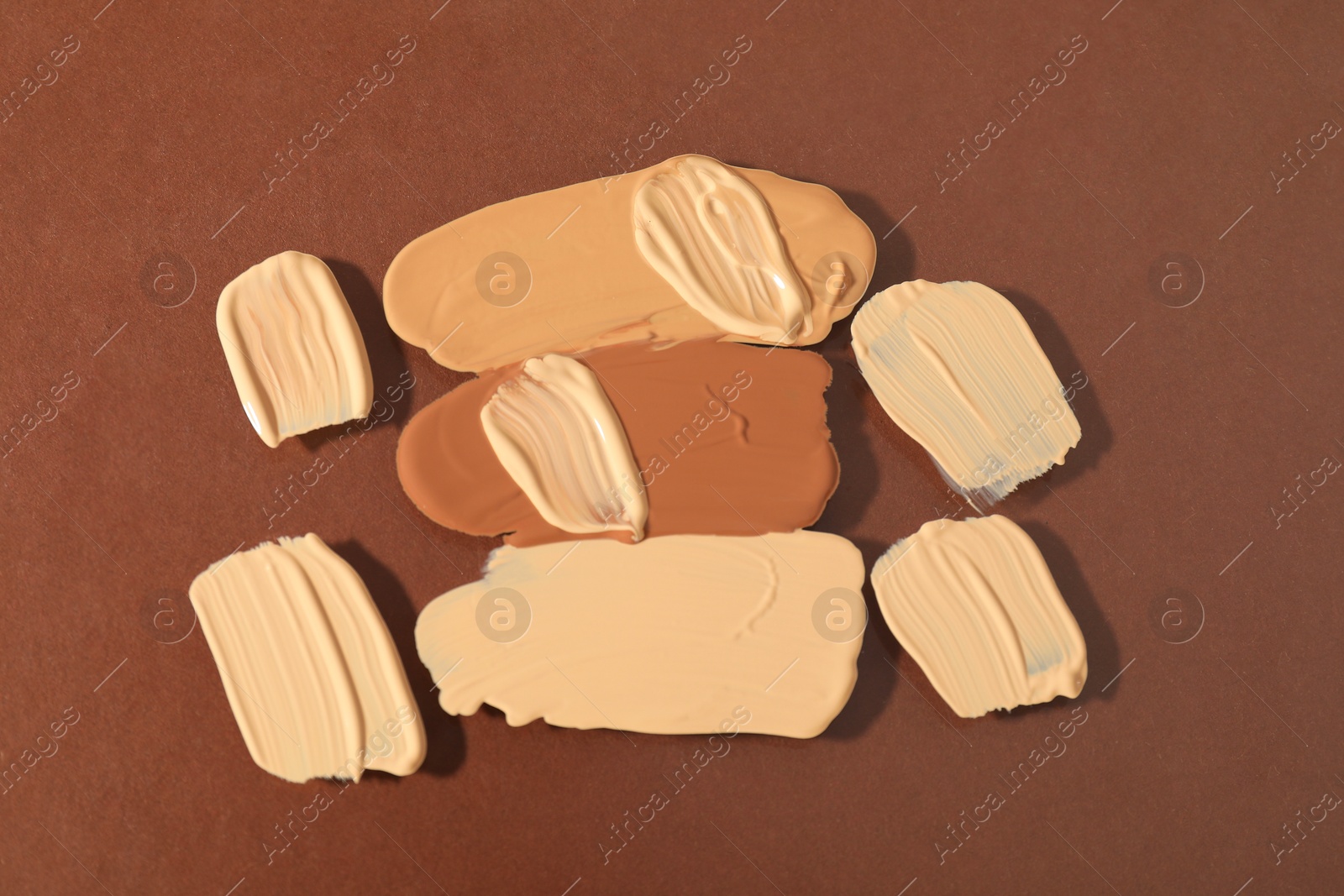 Photo of Samples of different foundations on brown background, top view