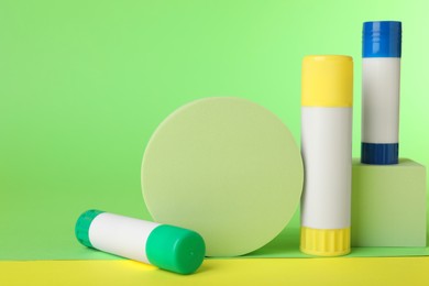 Photo of Glue sticks and podiums on light green background. Space for text