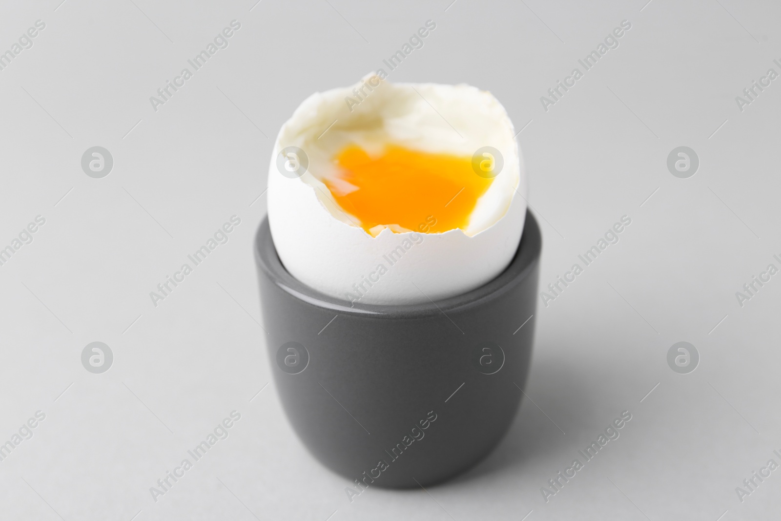 Photo of Soft boiled egg in cup on light grey background, closeup