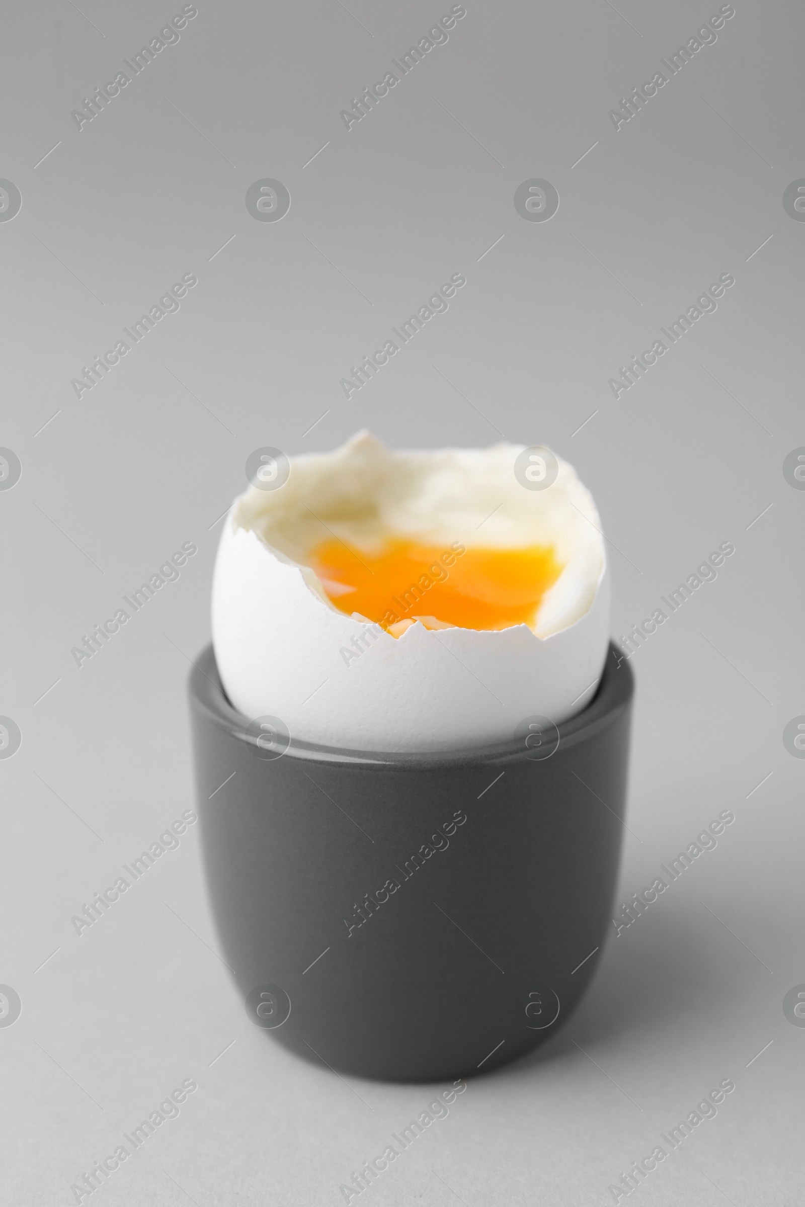 Photo of Soft boiled egg in cup on light grey background, closeup