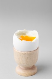 Photo of Soft boiled egg in cup on light grey background, closeup