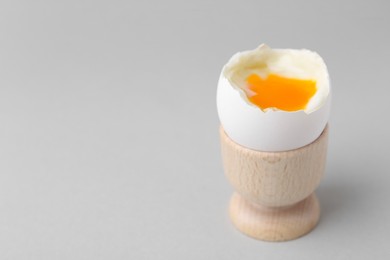 Soft boiled egg in cup on light grey background, space for text