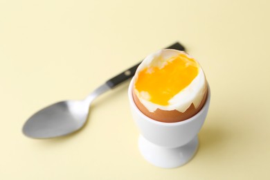 Photo of Soft boiled egg in eggcup and spoon on beige background, closeup