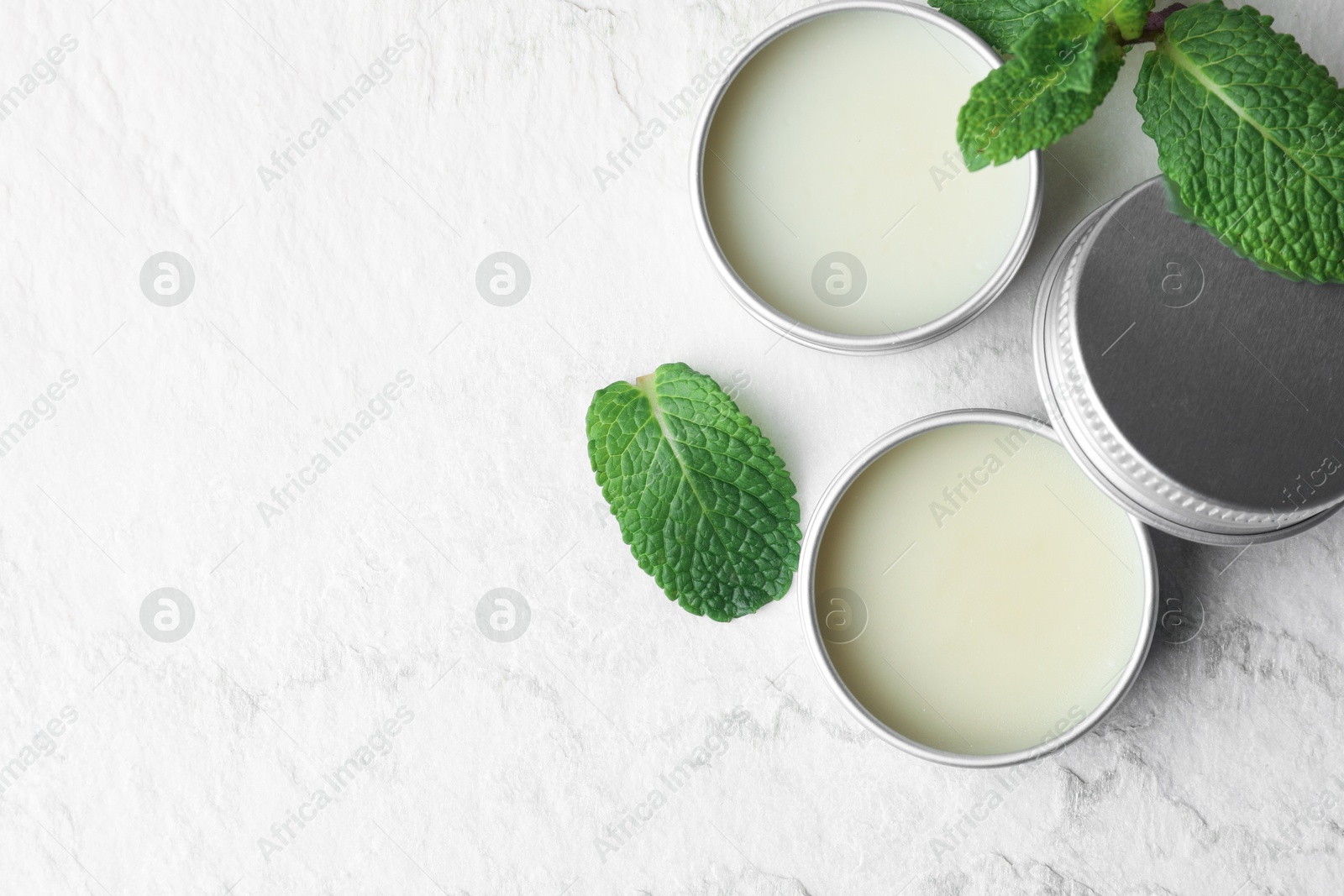 Photo of Mint lip balms and green leaves on beige textured background, flat lay. Space for text