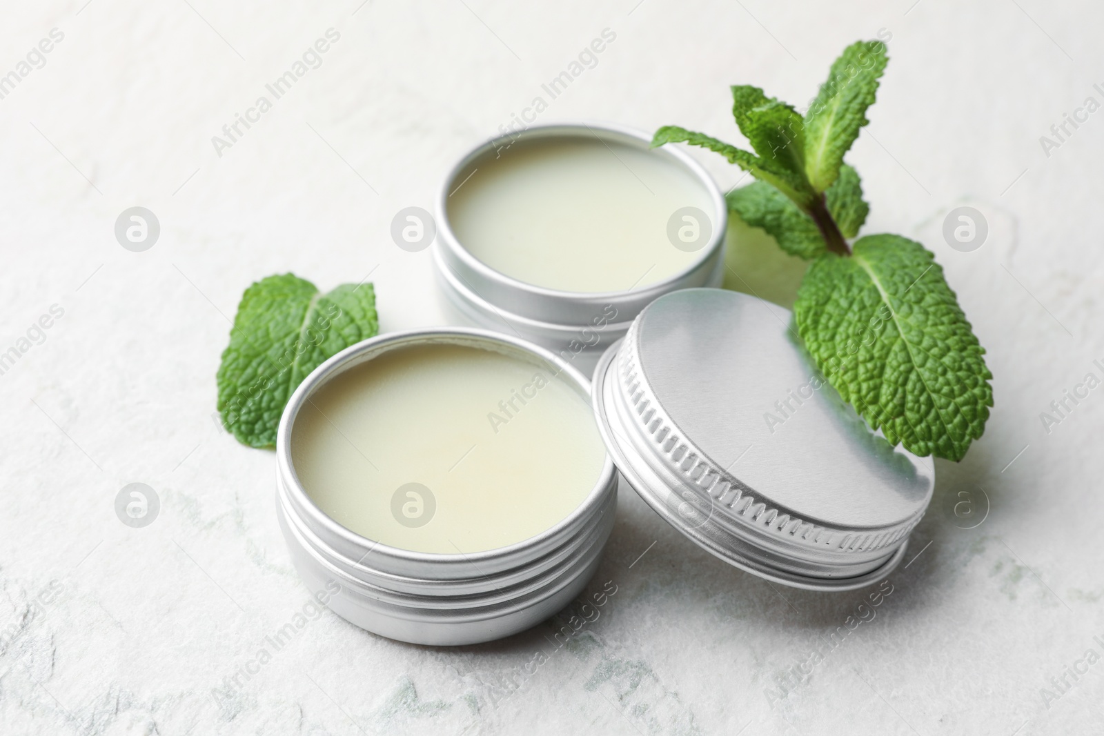 Photo of Mint lip balms and green leaves on beige textured table, closeup. Cosmetic product